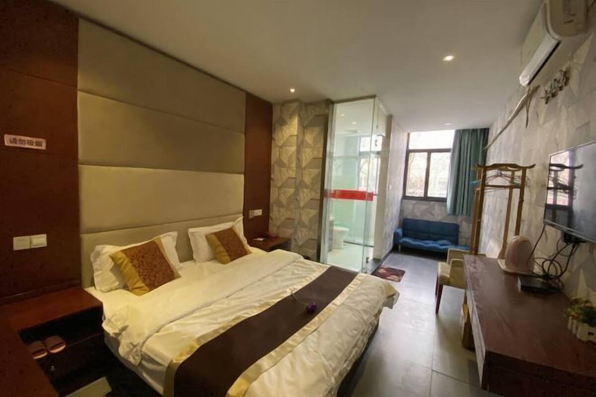 Une chambre d’hôtel avec un grand lit, un bureau avec une chaise, une télévision et une paroi en verre qui sépare la chambre de la salle de bain.
