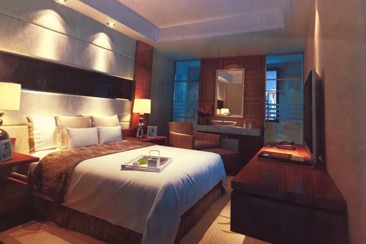 Una camera d'albergo con un letto grande, comodini, una scrivania con una sedia, televisore e uno specchio da bagno.