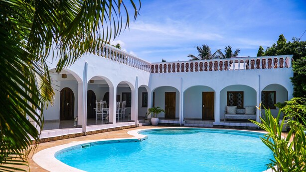 A poolside area with a white building featuring arched doorways and a tiled roof. - Diani Beach Villas - 3 Bedroom 50 meters to the Beach ⛱️🌴HOT!!
Kenya Coastal (Diani Beach)
