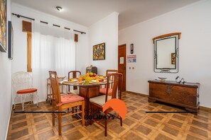 Un comedor con una mesa redonda, sillas y un frutero. Hay un aparador de madera y un espejo en la pared.