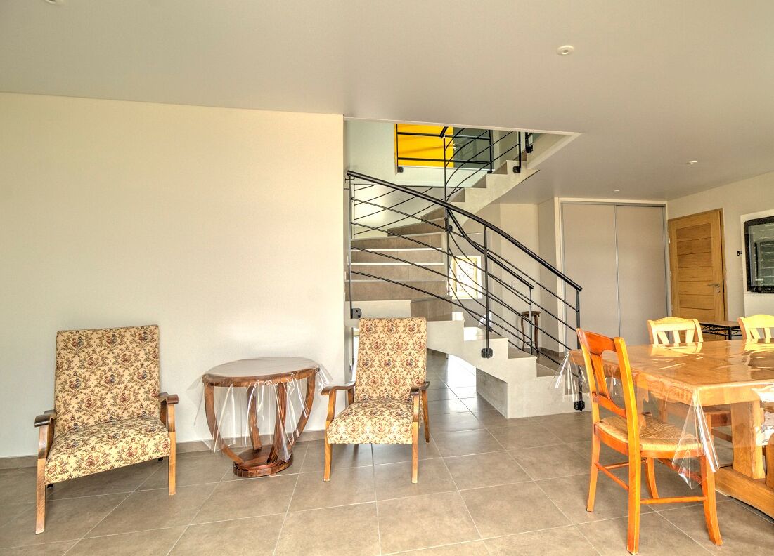 Un intérieur moderne comprenant un escalier, deux fauteuils à motifs, une table ronde et une table à manger avec des chaises.