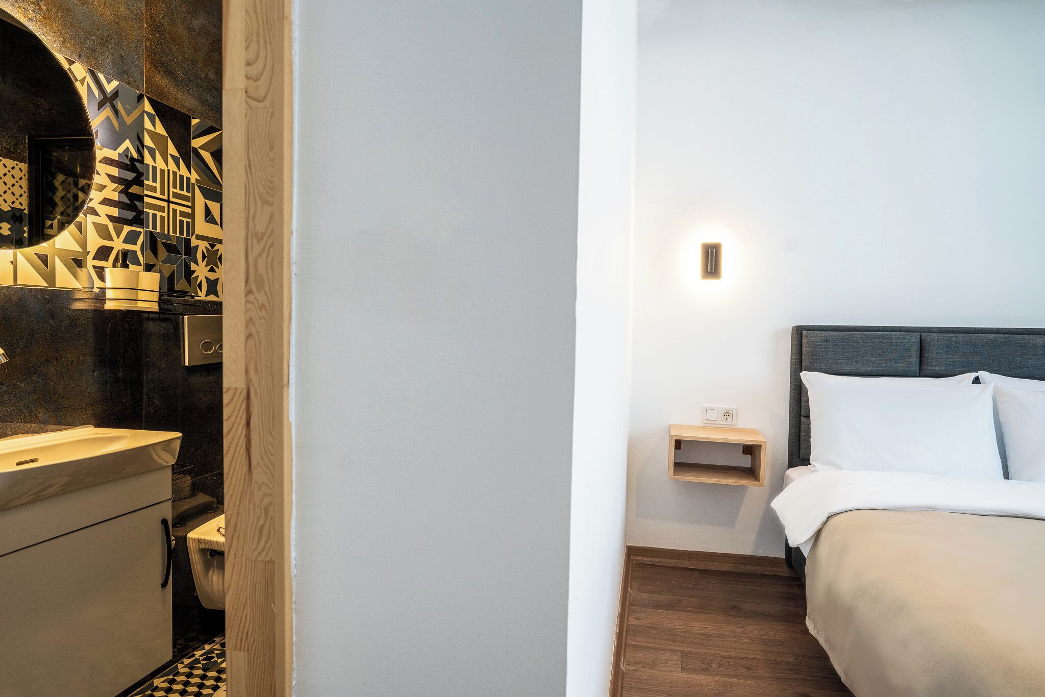 Une chambre d’hôtel comprenant un lit, une table de chevet, une commode, une lampe fixée au mur et un panneau décoratif mural.