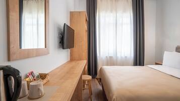 Une chambre d’hôtel avec un bureau en bois, une télévision, un lit et des rideaux.