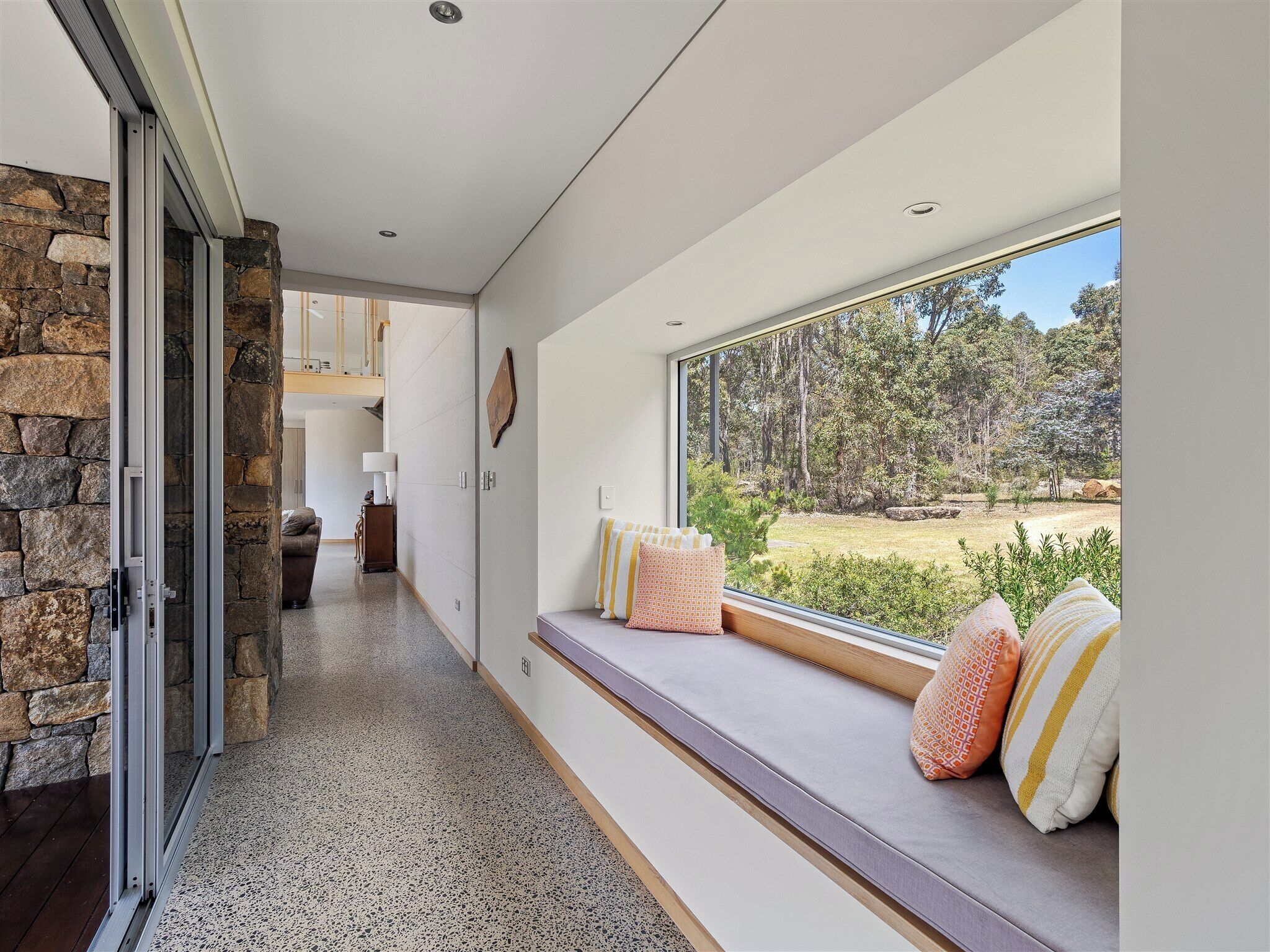 Interior moderno com parede de pedra, um banco com almofadas e vista para a paisagem natural.
