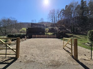 A gravel driveway leading to a wooden gate, surrounded by a fenced area with a building in the background.