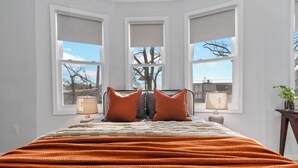 Un dormitorio con una cama grande, tres ventanas y vistas a la ciudad.