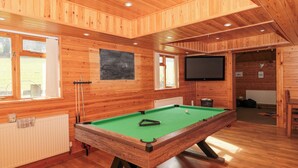 A wooden room with a pool table, a television, and windows.