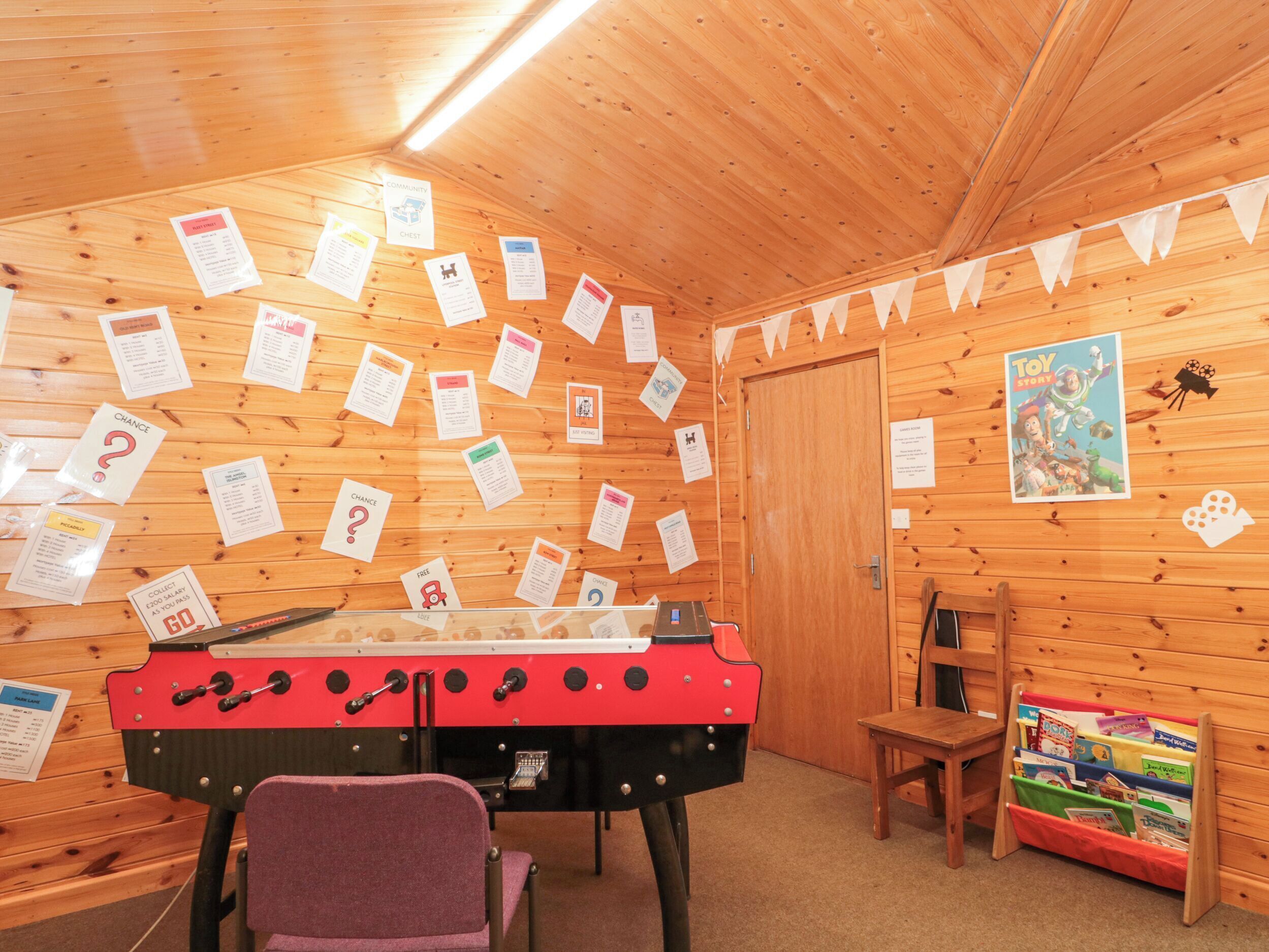 A cozy room with wooden walls, a red and black foosball table, a purple chair, and a bookshelf filled with children's books.
