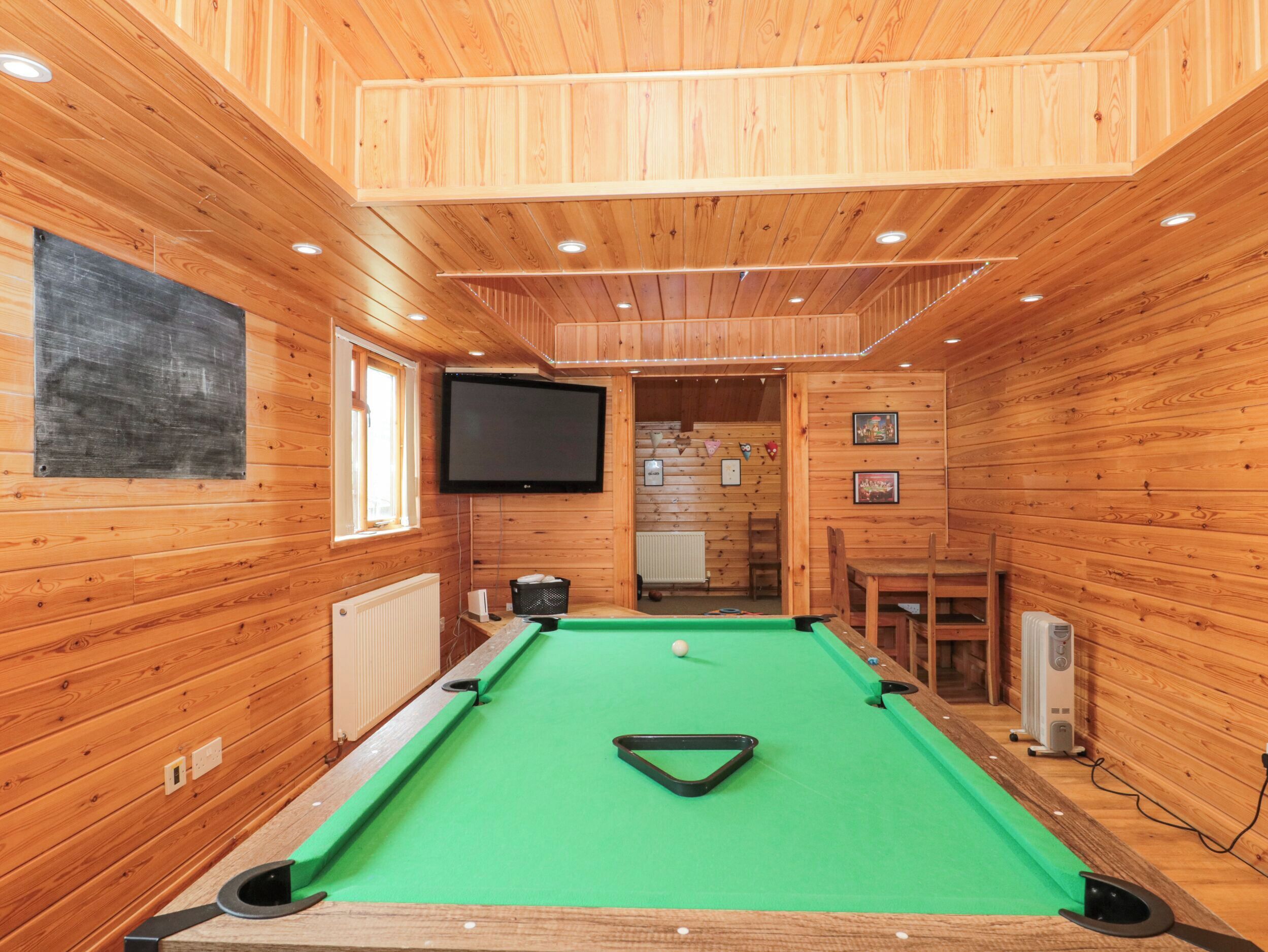 A wooden-paneled room with a pool table, a television, and a radiator.