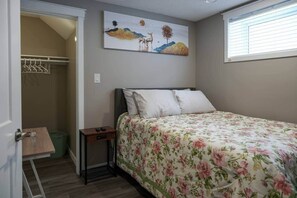 A bedroom with a bed, a nightstand, a closet, and a painting on the wall. - Elegant Family Suite by Stadium, Airport, Shopping (Regina)