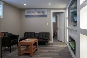 A modern living room with a sofa, a coffee table, and a painting on the wall. - Elegant Family Suite by Stadium, Airport, Shopping (Regina)