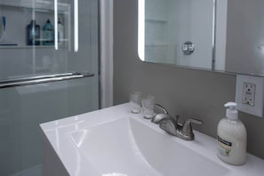 A modern bathroom with a white sink, a mirror, and a shower area.