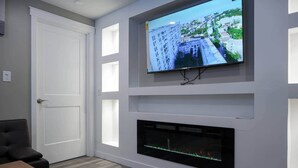 A modern living room with a flat-screen TV mounted on the wall, a fireplace below it, and a door to the left.