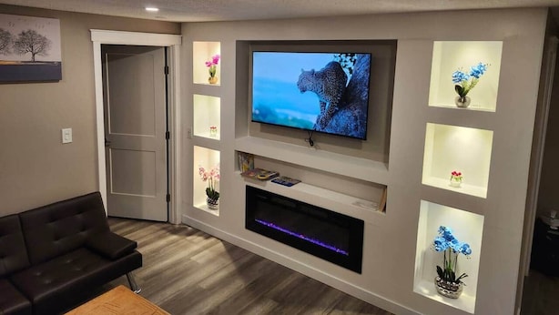 A modern living room with a flat-screen TV mounted on the wall, surrounded by shelves with decorative items and a built-in entertainment unit.