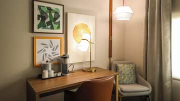 A hotel room with a wooden desk, a coffee maker, a lamp, and a chair.