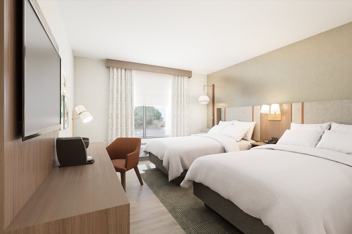 Een hotelkamer met twee bedden, een bureau, een stoel en een televisie.