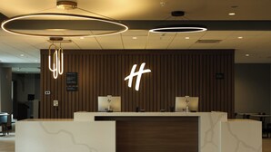 A modern reception desk with a wooden panel backdrop and two monitors. - Holiday Inn Osceola by IHG (Osceola)