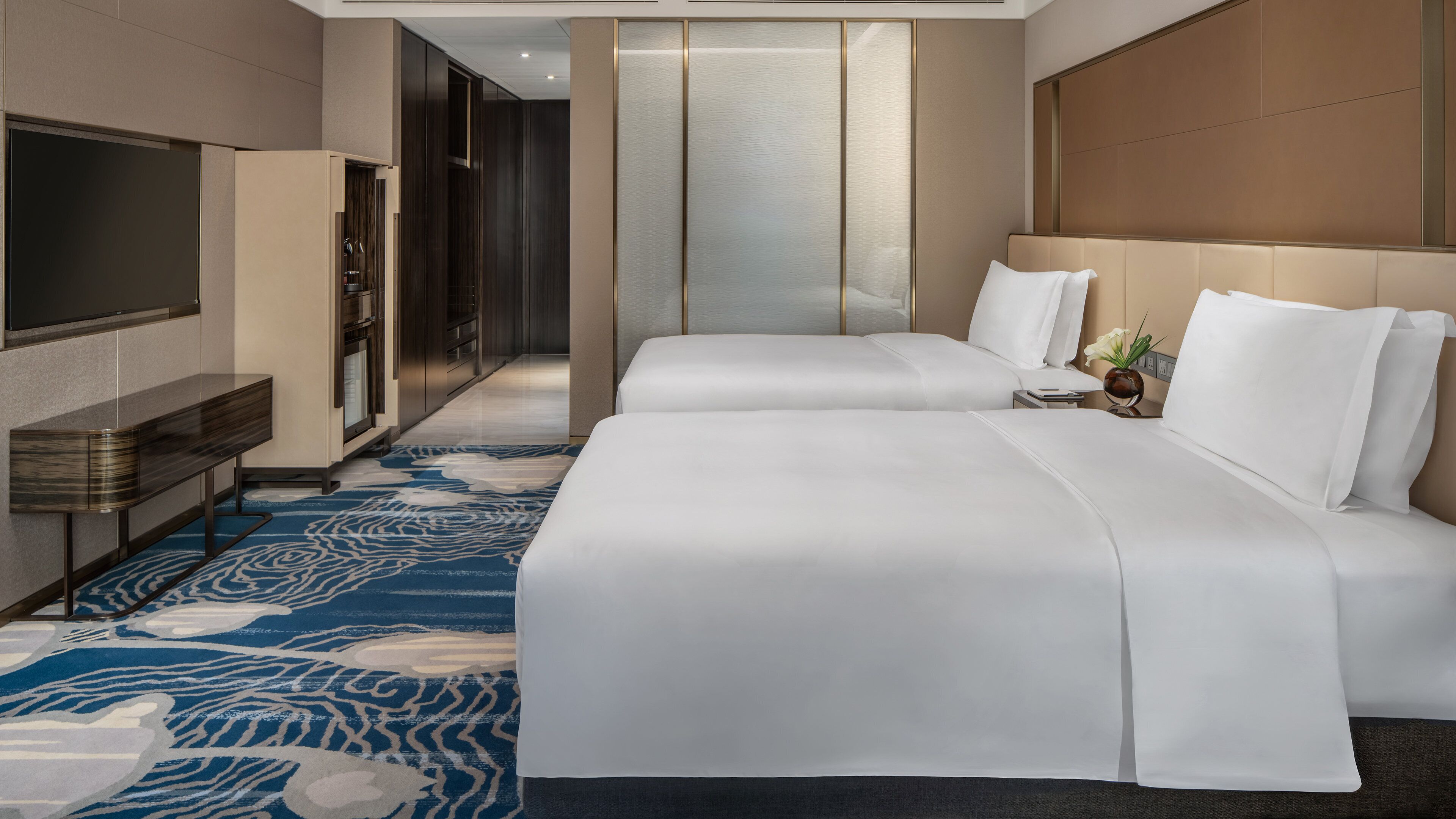 A hotel room with a large bed, a TV, a desk, and a patterned carpet.