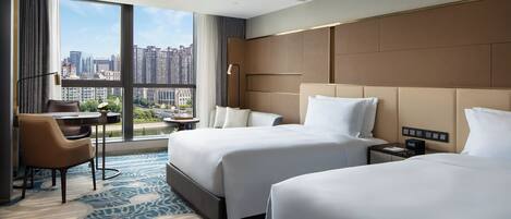 A hotel room with two beds, a desk, a chair, a large window with a city view, and a modern design.