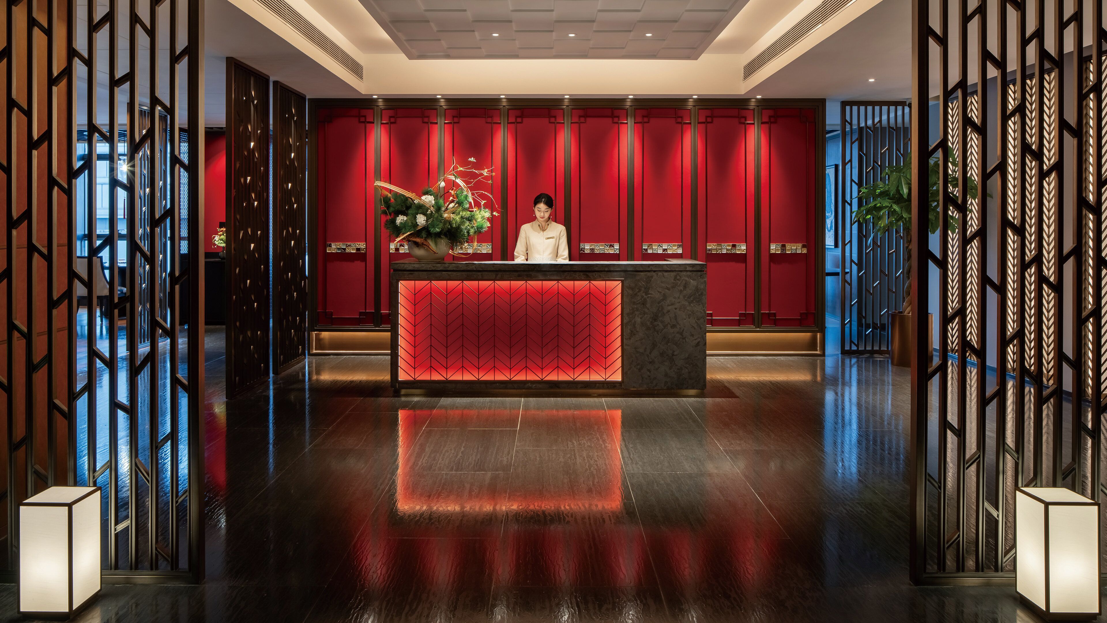 A reception area with a red backdrop, a receptionist, and a decorative plant.
