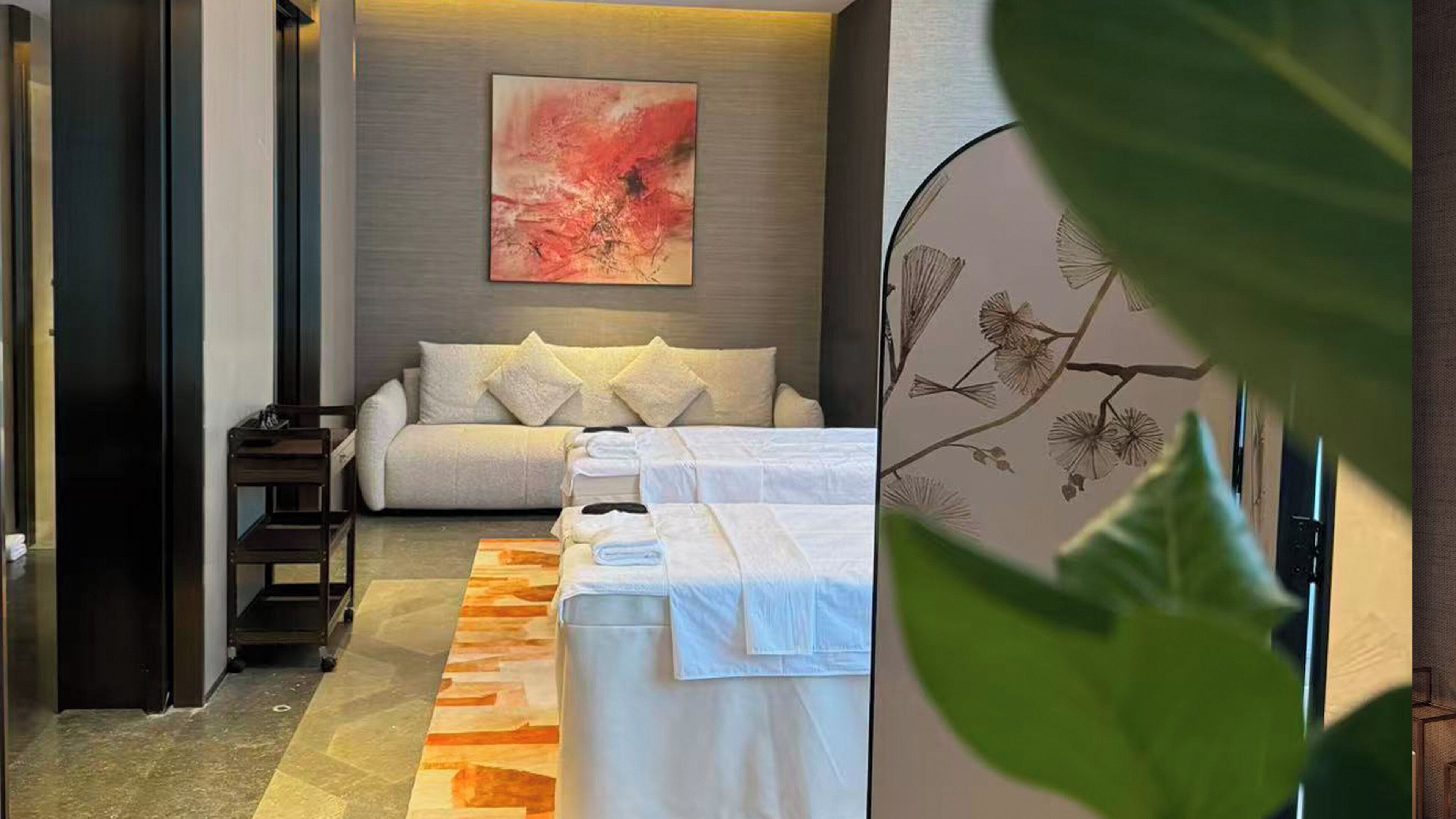 A hotel room with a sofa, a bed, a painting, and a plant.