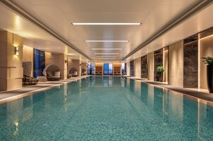 Una piscina interior amplia con suelo de baldosas, rodeada de paredes con grandes ventanales e iluminación moderna.