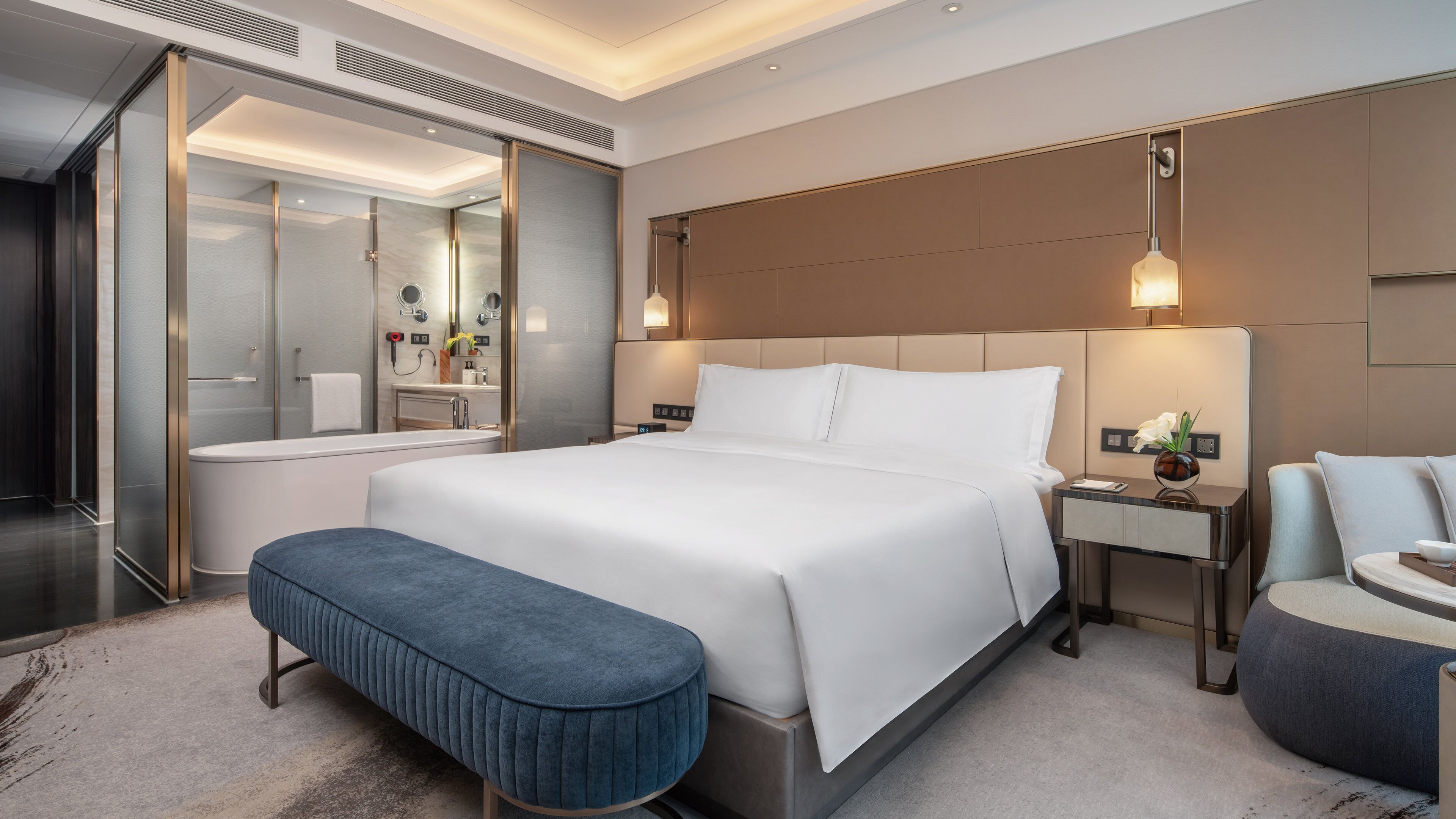 Ein modernes Hotelzimmer mit einem großen Bett, einem eigenen Badezimmer, einer Sitzecke und einem Nachttisch mit Lampe.