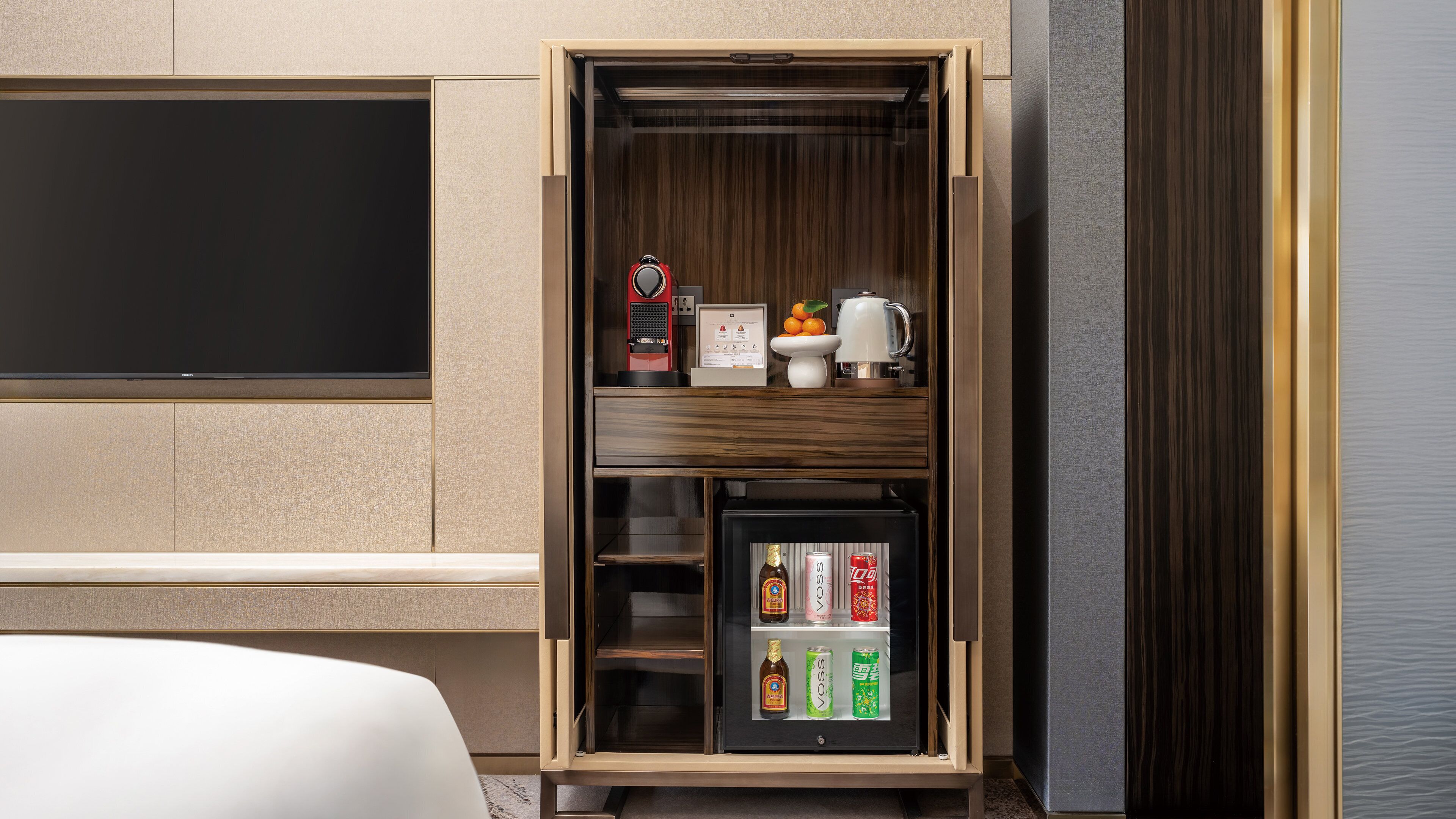 A minibar with a coffee machine, a small refrigerator with beverages, and a fruit bowl.