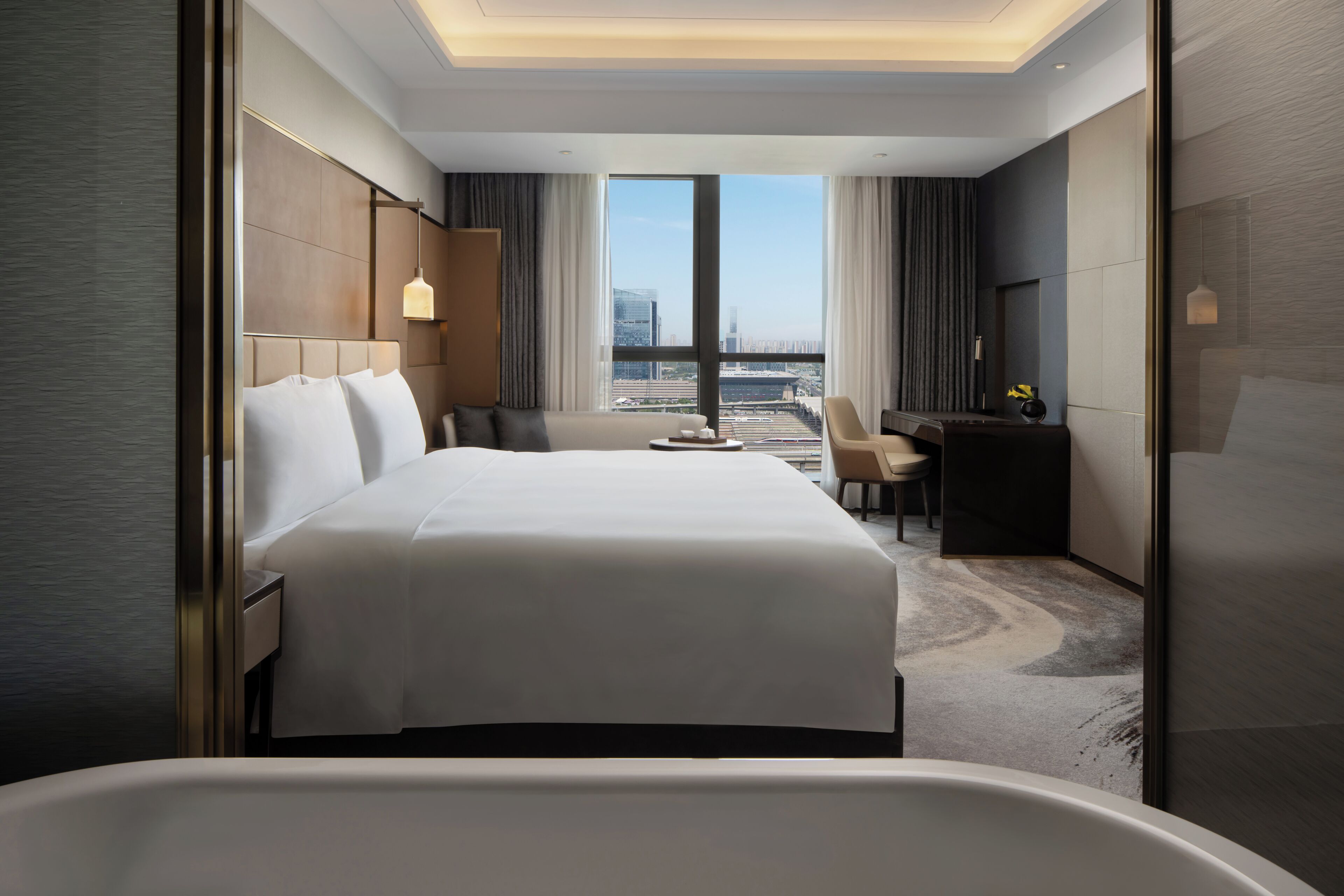 Habitación de hotel moderna con una cama grande, un escritorio, una silla y vistas a la ciudad.