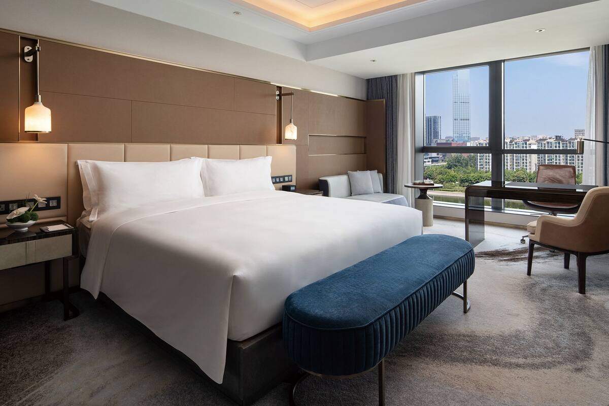 Une chambre d’hôtel moderne dotée d’un grand lit, d’un bureau avec un piano, d’une vue sur la ville et d’une grande fenêtre.