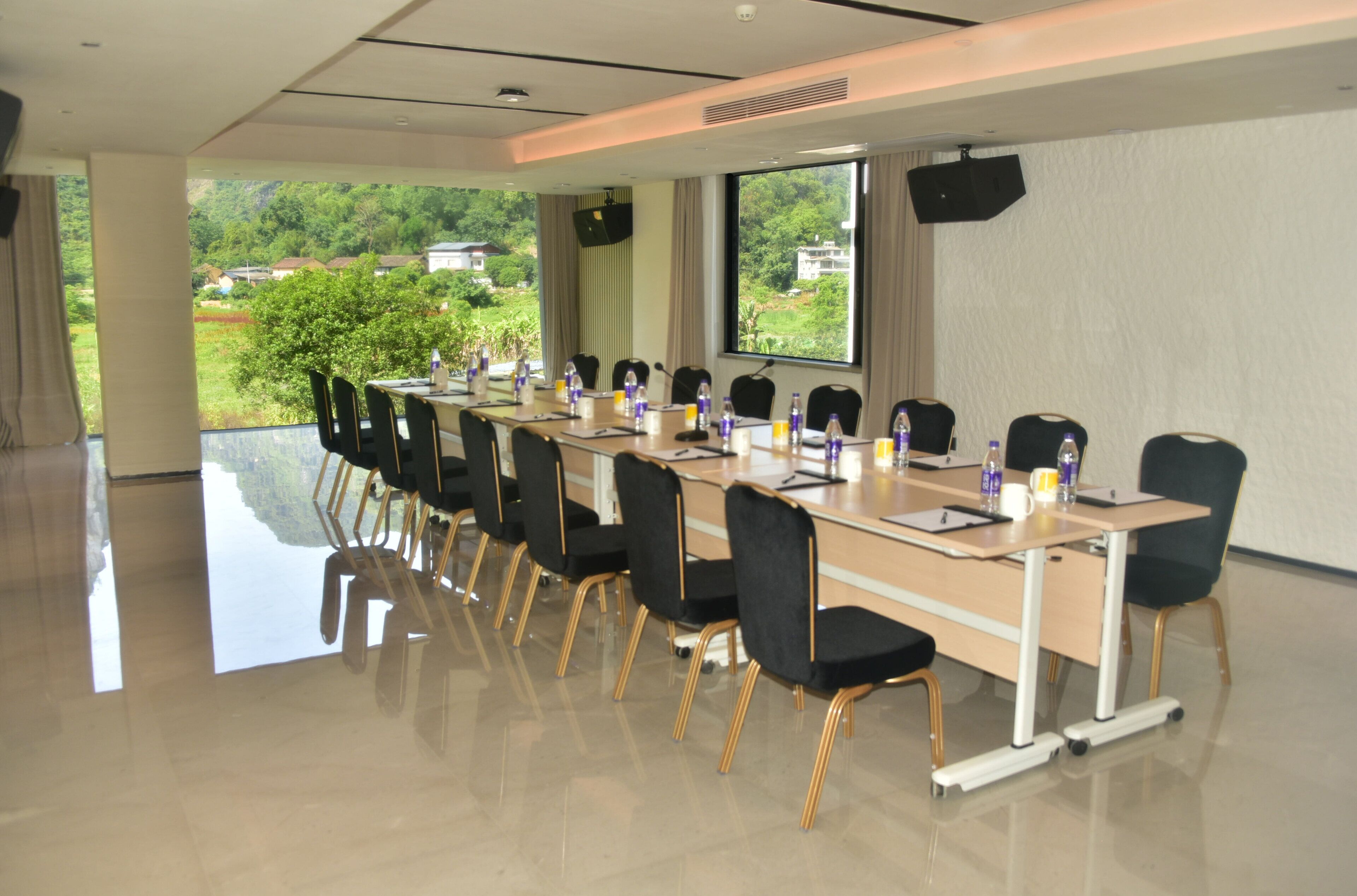 A conference room with a long table, chairs, and a large window offering a view of greenery and buildings.