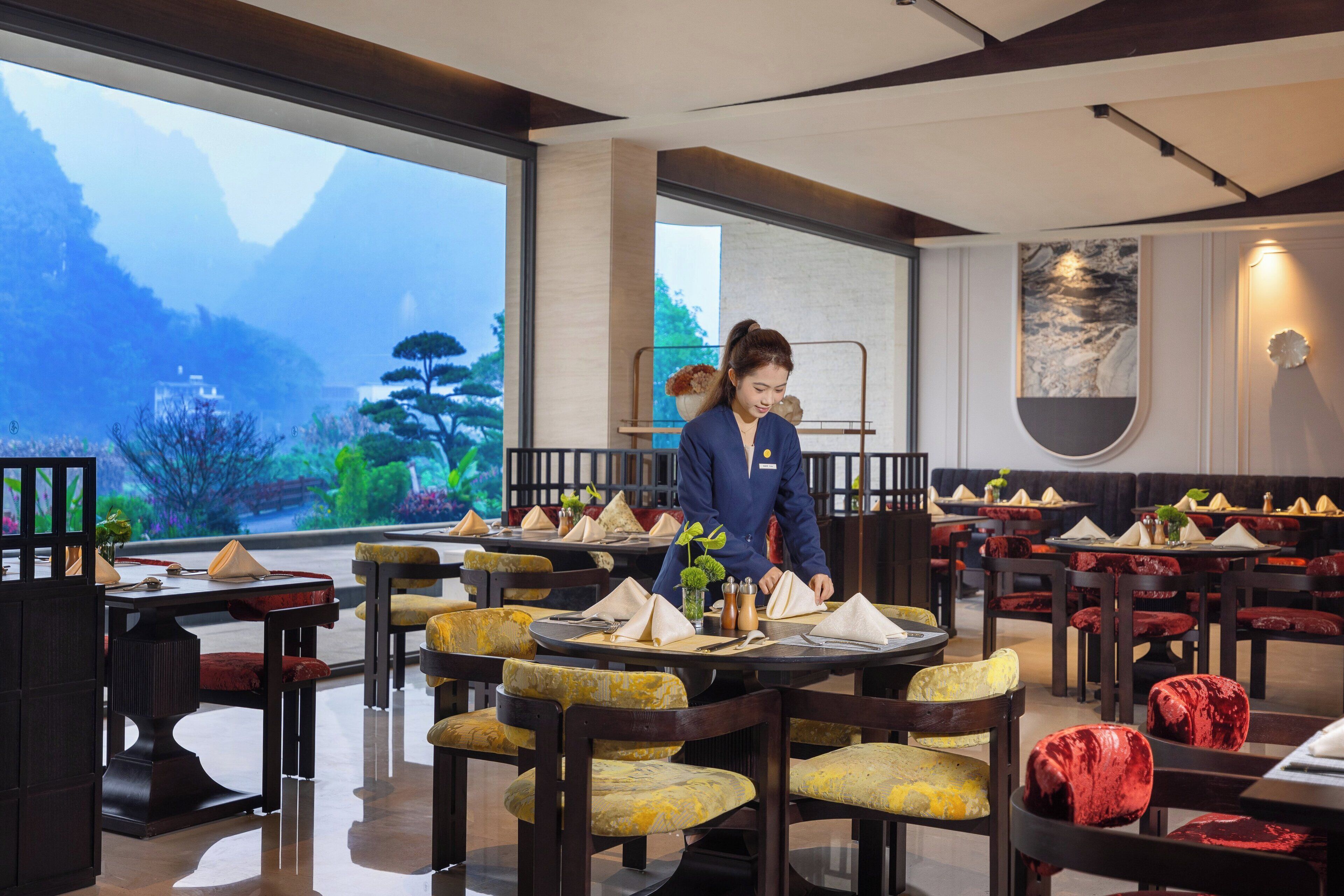 Un restaurante con mesas y sillas de madera, vistas a montañas a través de amplios ventanales y un diseño de interiores moderno.