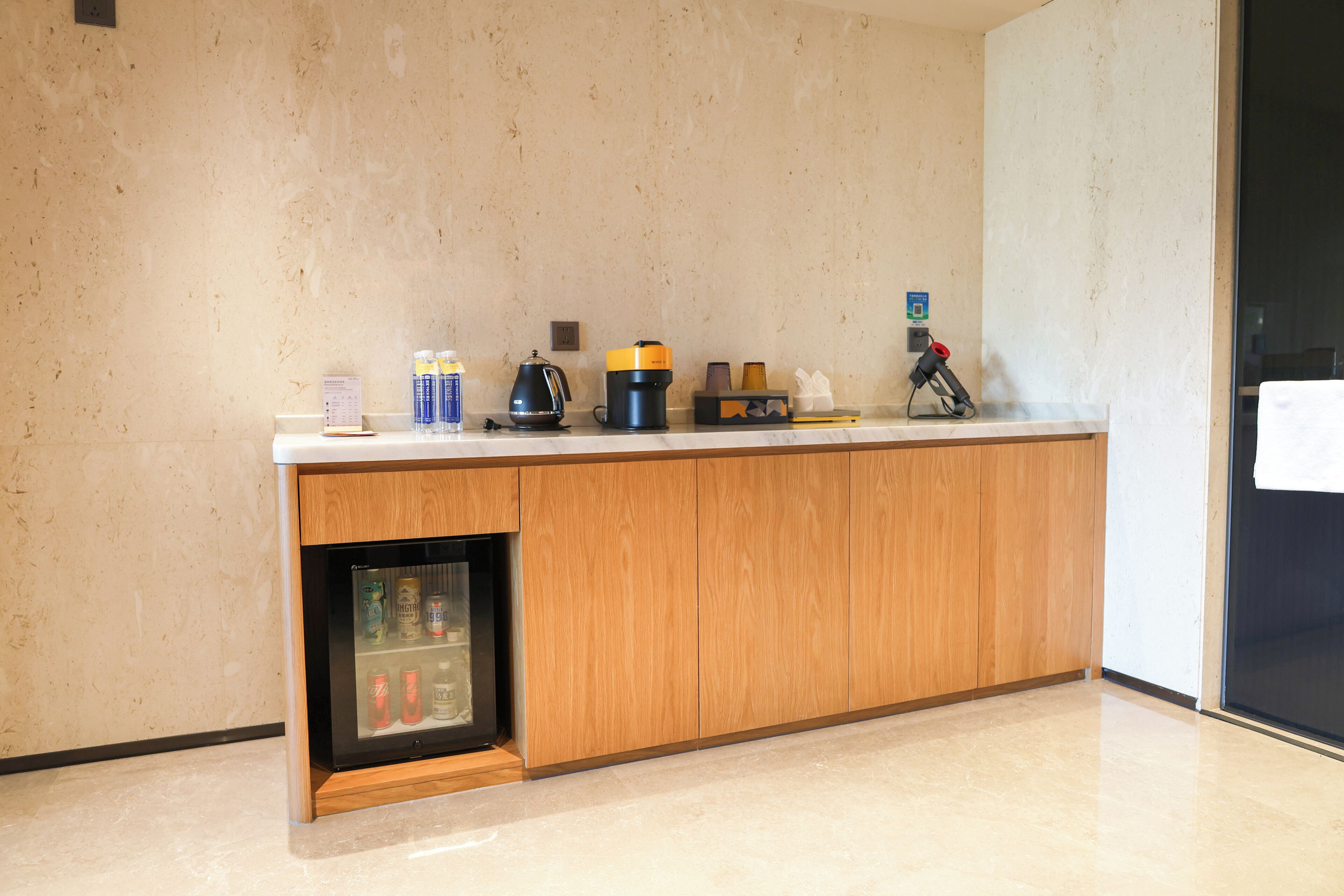 A kitchenette with a refrigerator, coffee maker, and various beverages.