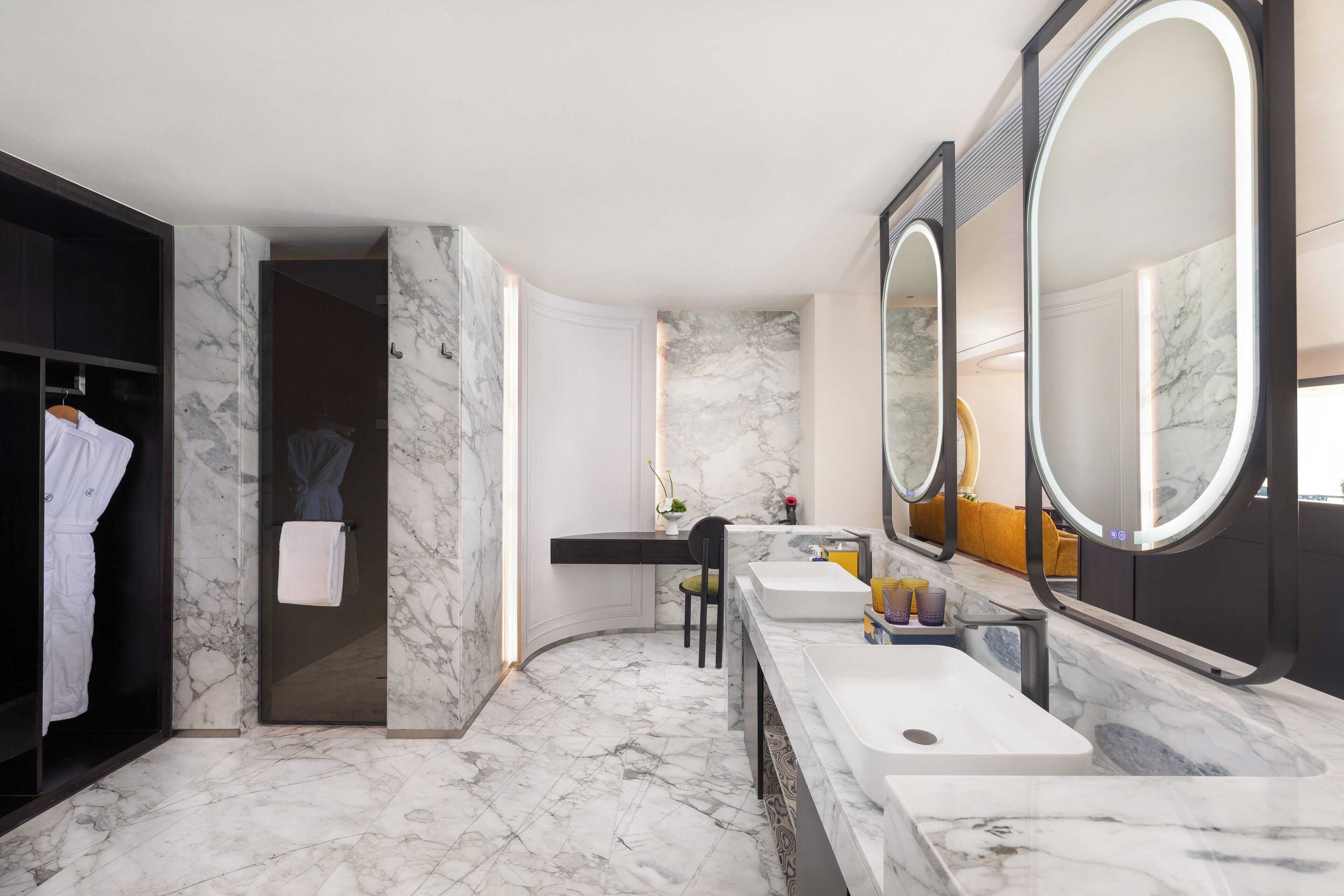 A modern bathroom with marble flooring, a walk-in shower, a vanity with a large mirror, and a robe rack.