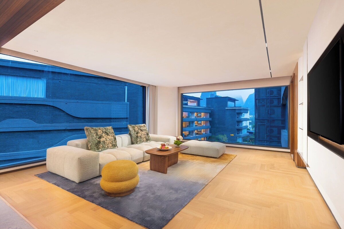 A modern living room with a large window, a sofa set, a coffee table, and a TV.