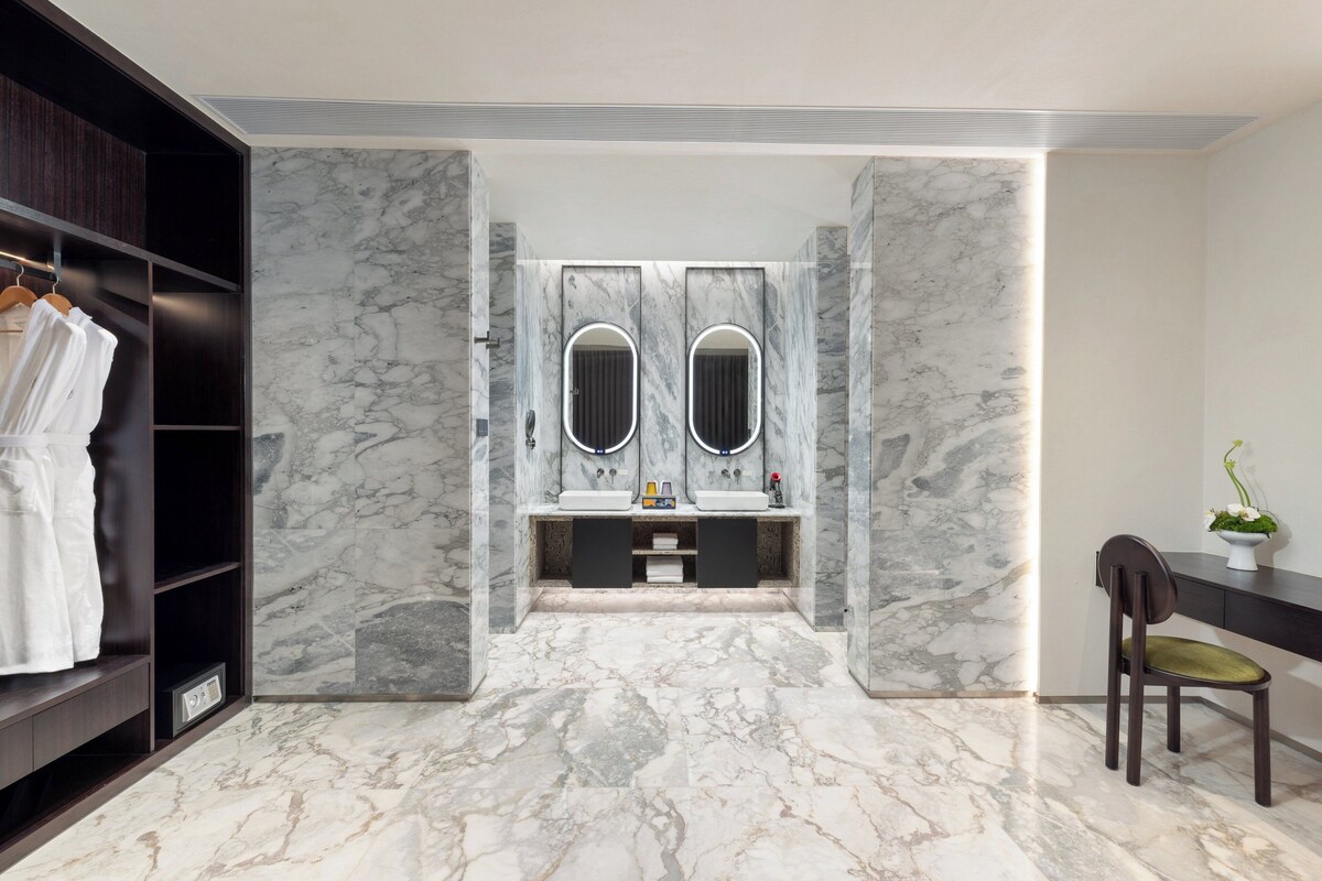 A modern bathroom with marble walls, two sinks with mirrors, a vanity, and a chair.