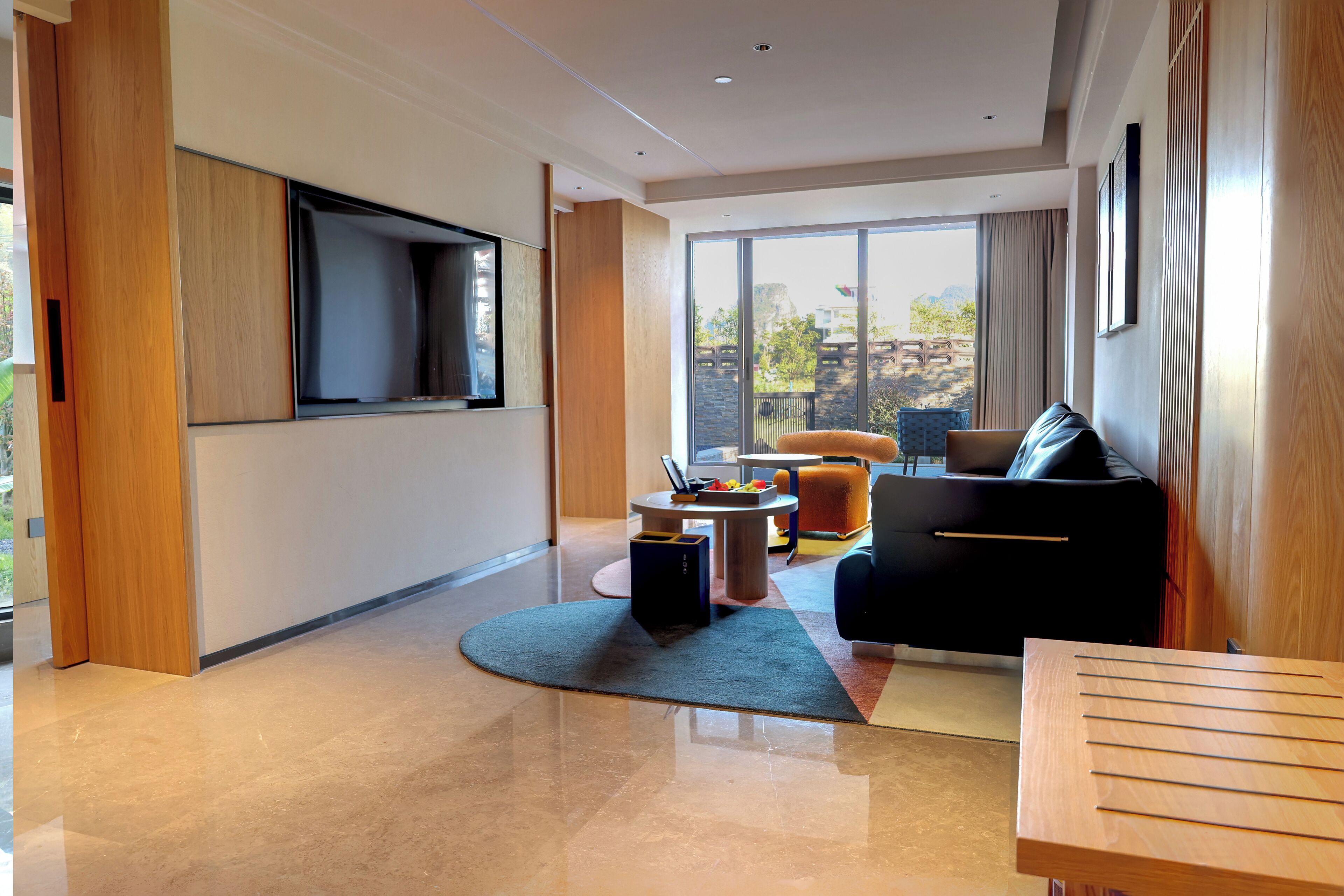 A modern living room with a large TV, a sofa, a coffee table, and a view of the outdoors.
