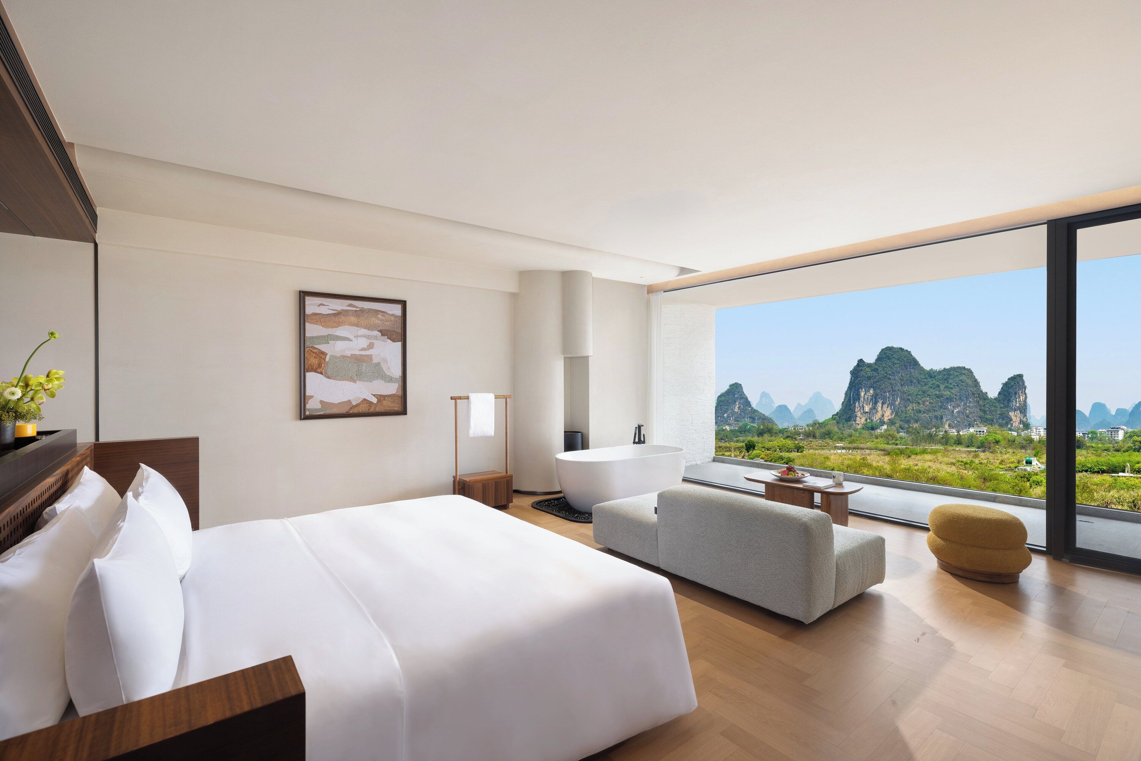 Una habitación de hotel moderna con una cama grande, un sofá, una bañera y vistas a las montañas.