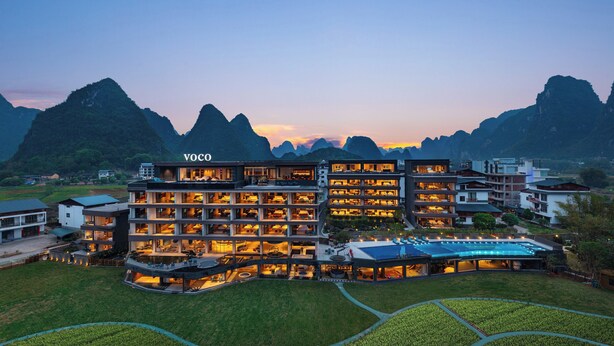 A multi-story hotel with a modern design, featuring a swimming pool and surrounded by mountainous terrain. - voco Guilin Yangshuo by IHG (Guilin)