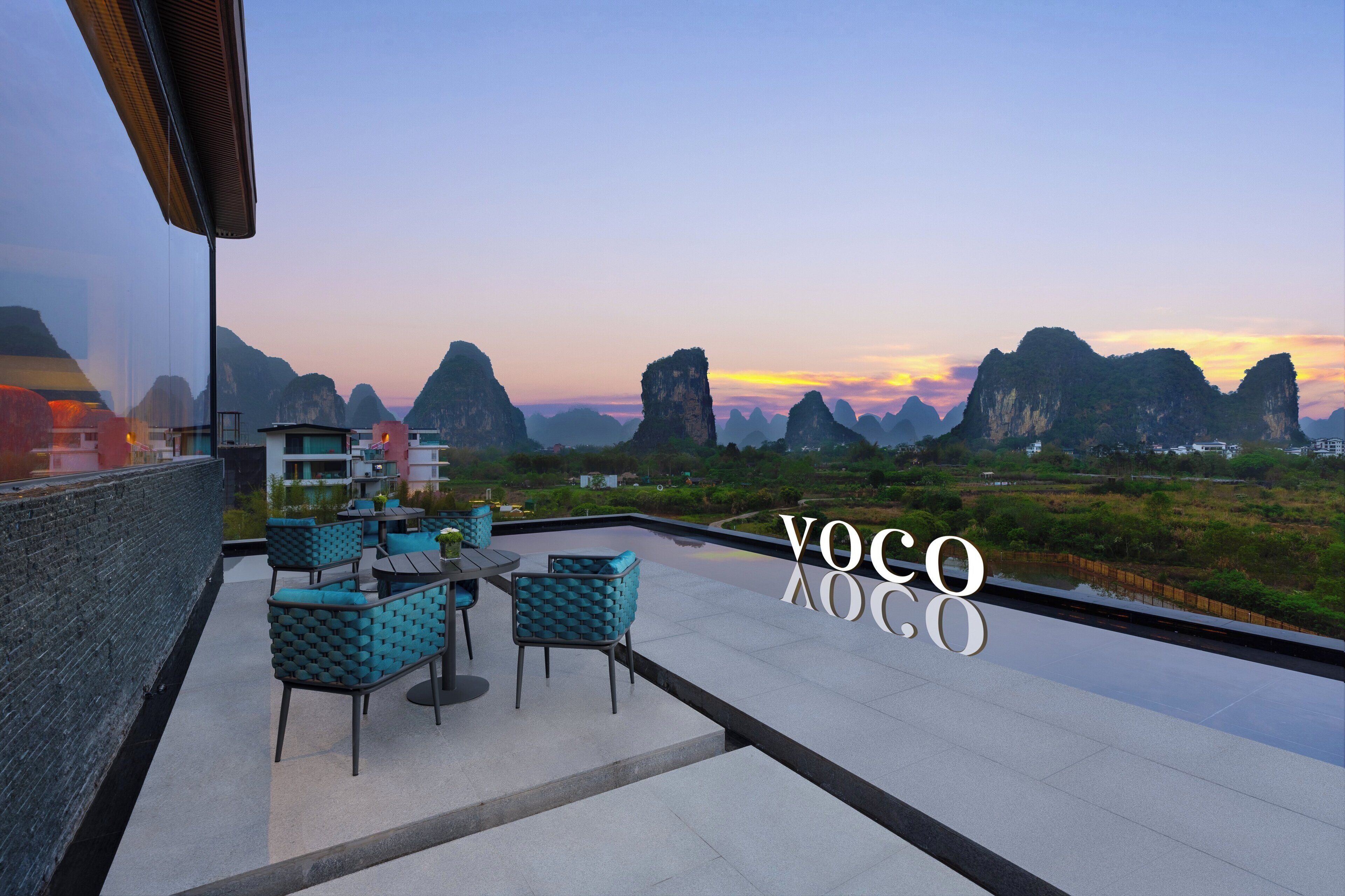 A rooftop terrace with outdoor seating, a view of karst mountains, and the text "YOCO XCO".
