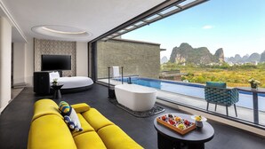 A modern living room with a large sofa, a flat-screen TV, a bathtub, and a dining table with fruit. - voco Guilin Yangshuo by IHG (Guilin)