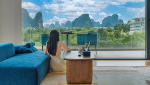 A room with a large window, a blue sofa, a wooden coffee table, and a view of natural scenery. - voco Guilin Yangshuo by IHG (Guilin)