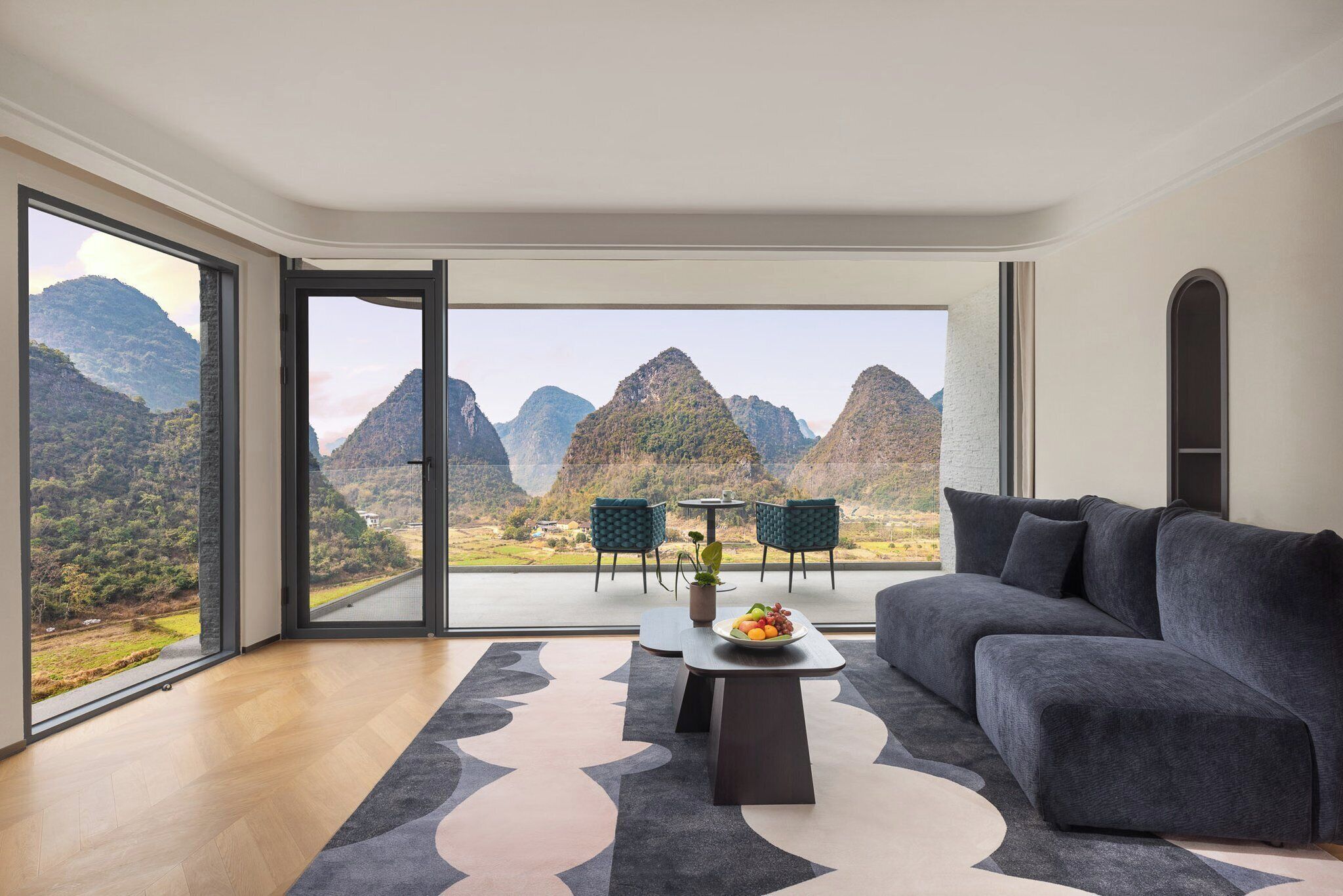 Un salon moderne avec un grand canapé, une table basse sur laquelle sont disposés des fruits, et une vue sur les montagnes grâce à de grandes fenêtres.