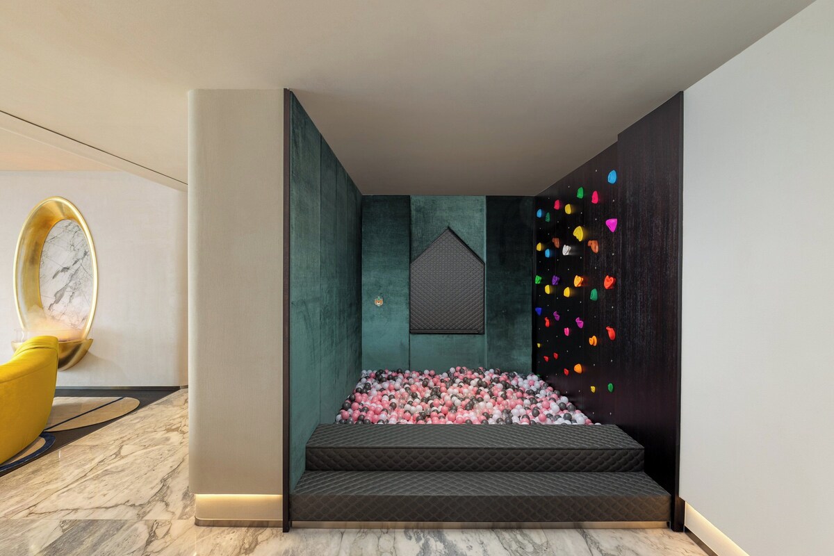 A modern room with teal walls, a marble floor, a bed with pink and gray pillows, and a colorful wall decoration.