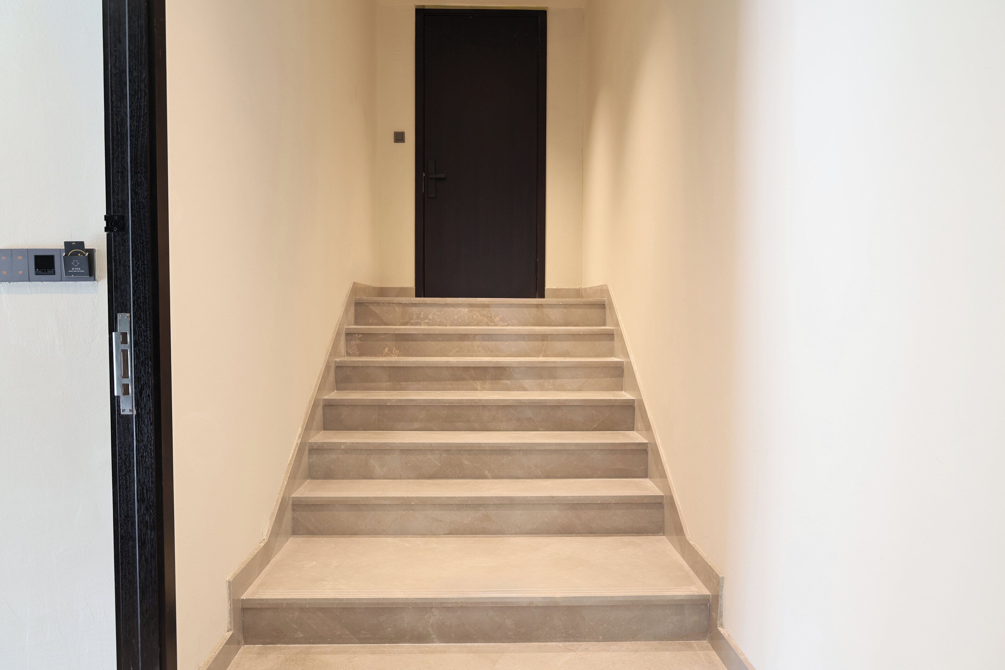 Eine Treppe führt zu einer schwarzen Tür in einem Korridor mit weißen Wänden.