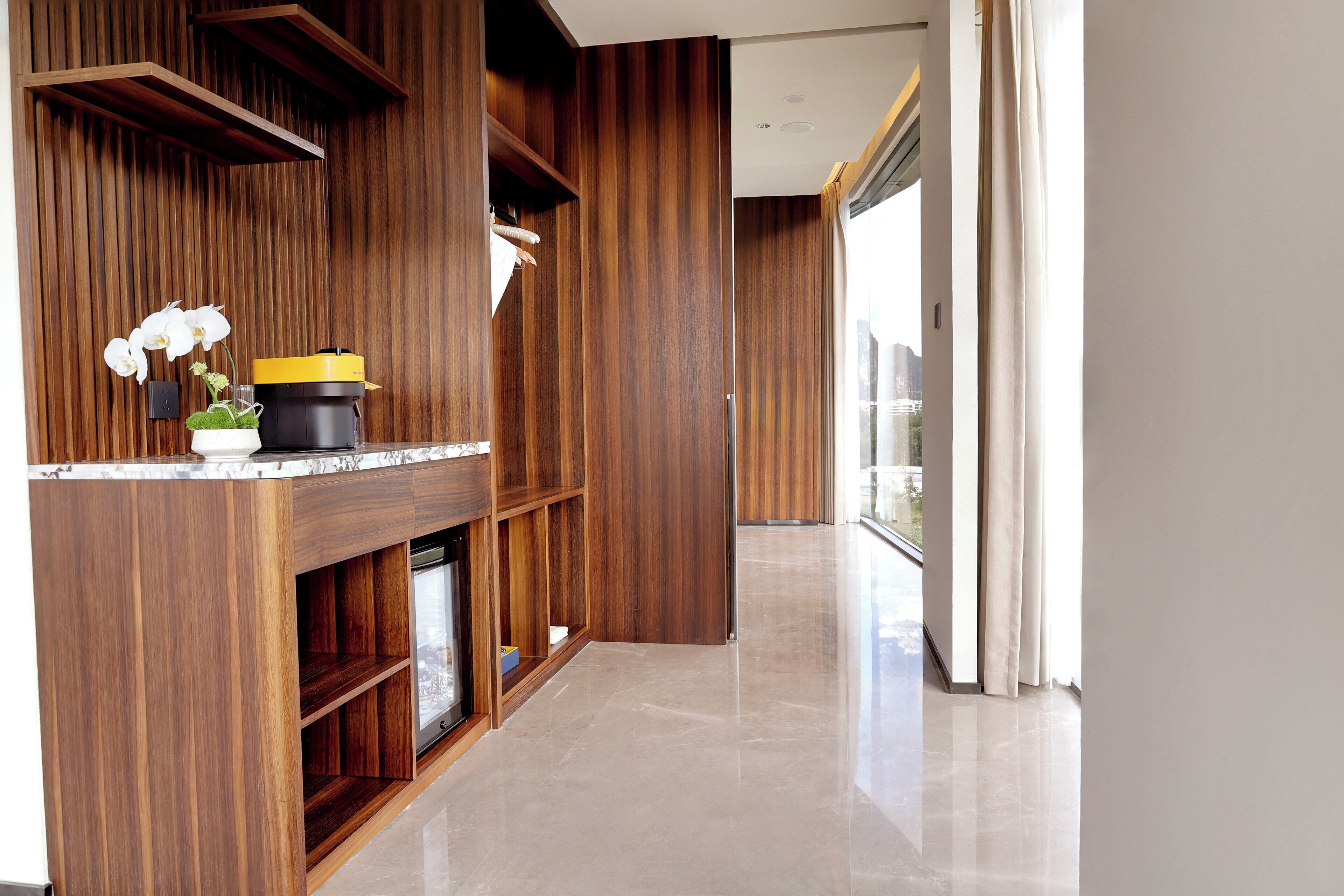 A modern kitchen with wooden cabinetry, a marble countertop, and a potted orchid.