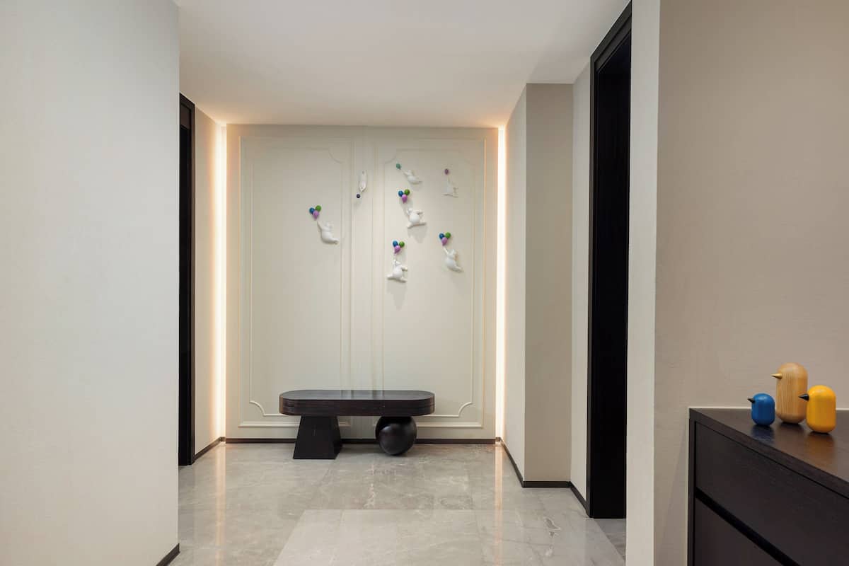 A modern hallway with a bench, a wall-mounted art installation, and a small table with decorative items.