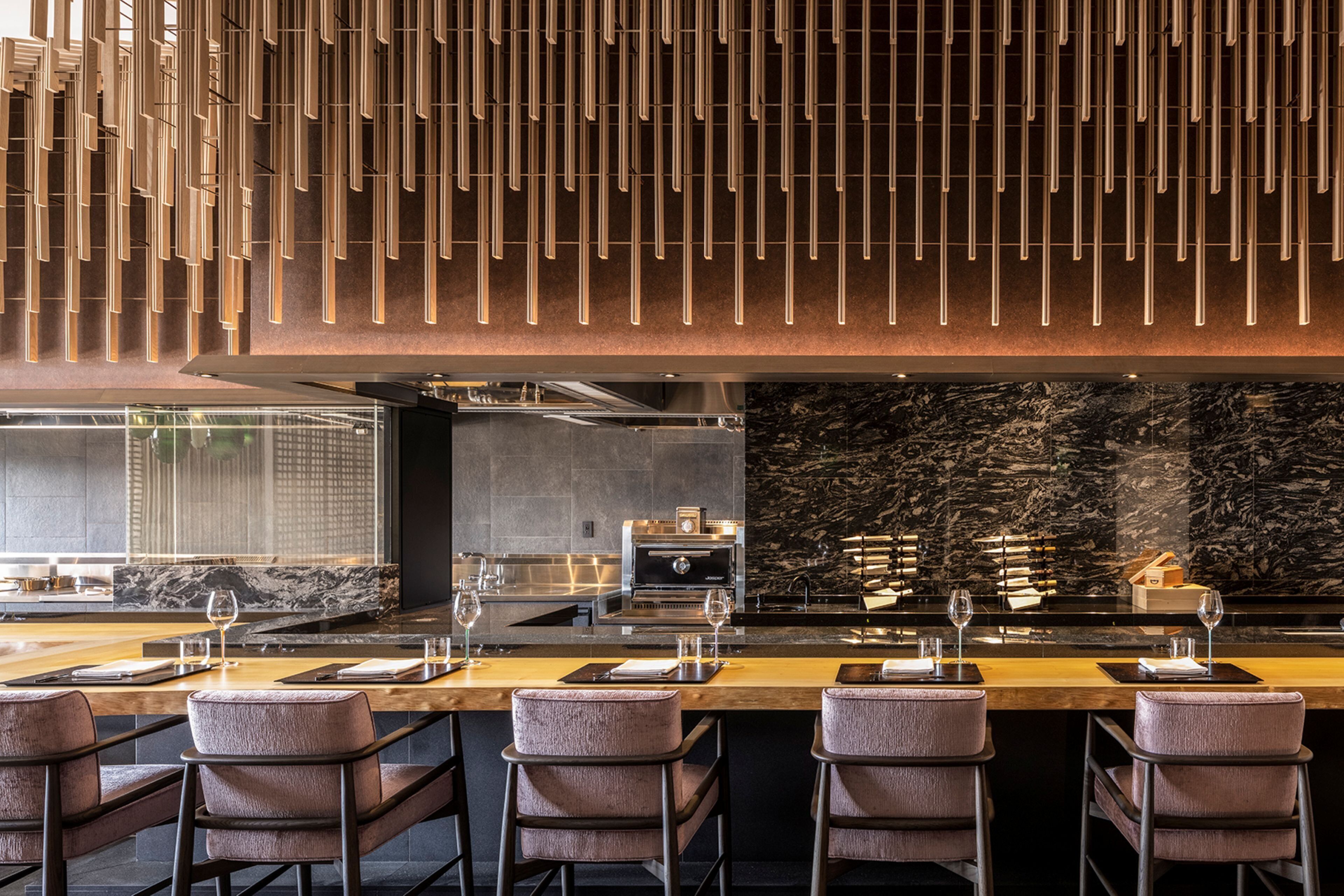 A modern bar area with a long counter, multiple bar stools, and a decorative hanging light fixture.