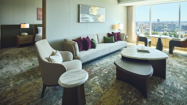 A modern hotel room with a large window offering a city view, a sofa with colorful cushions, a small side table, and a round coffee table. - InterContinental Sapporo by IHG (Sapporo)