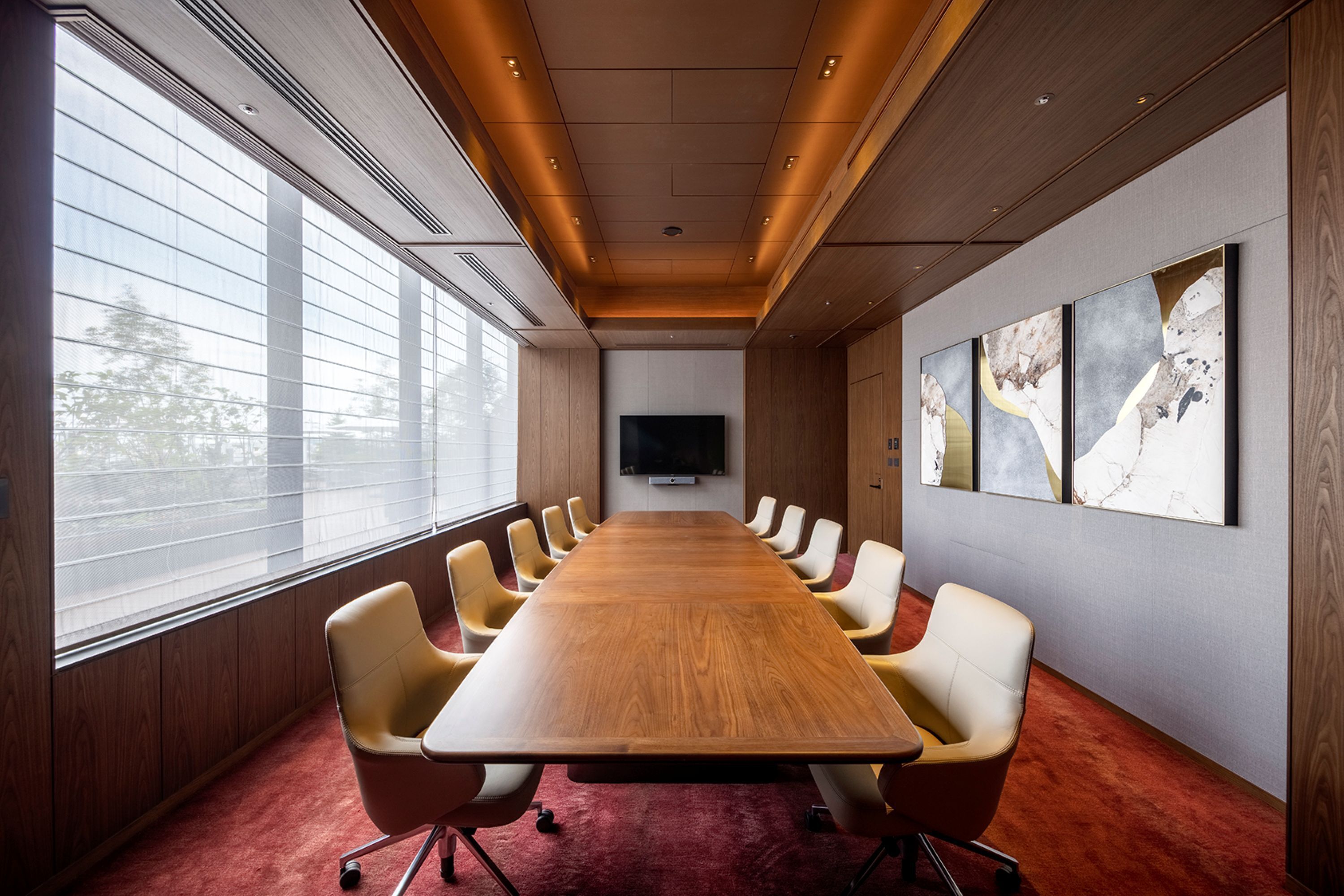 A conference room with a long wooden table, yellow chairs, a TV on the wall, and large windows.